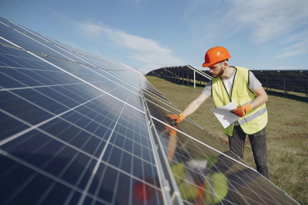 pexels-photo-4254171-4254171 Technician in PPE inspects solar panels in a renewable energy field, promoting sustainability.